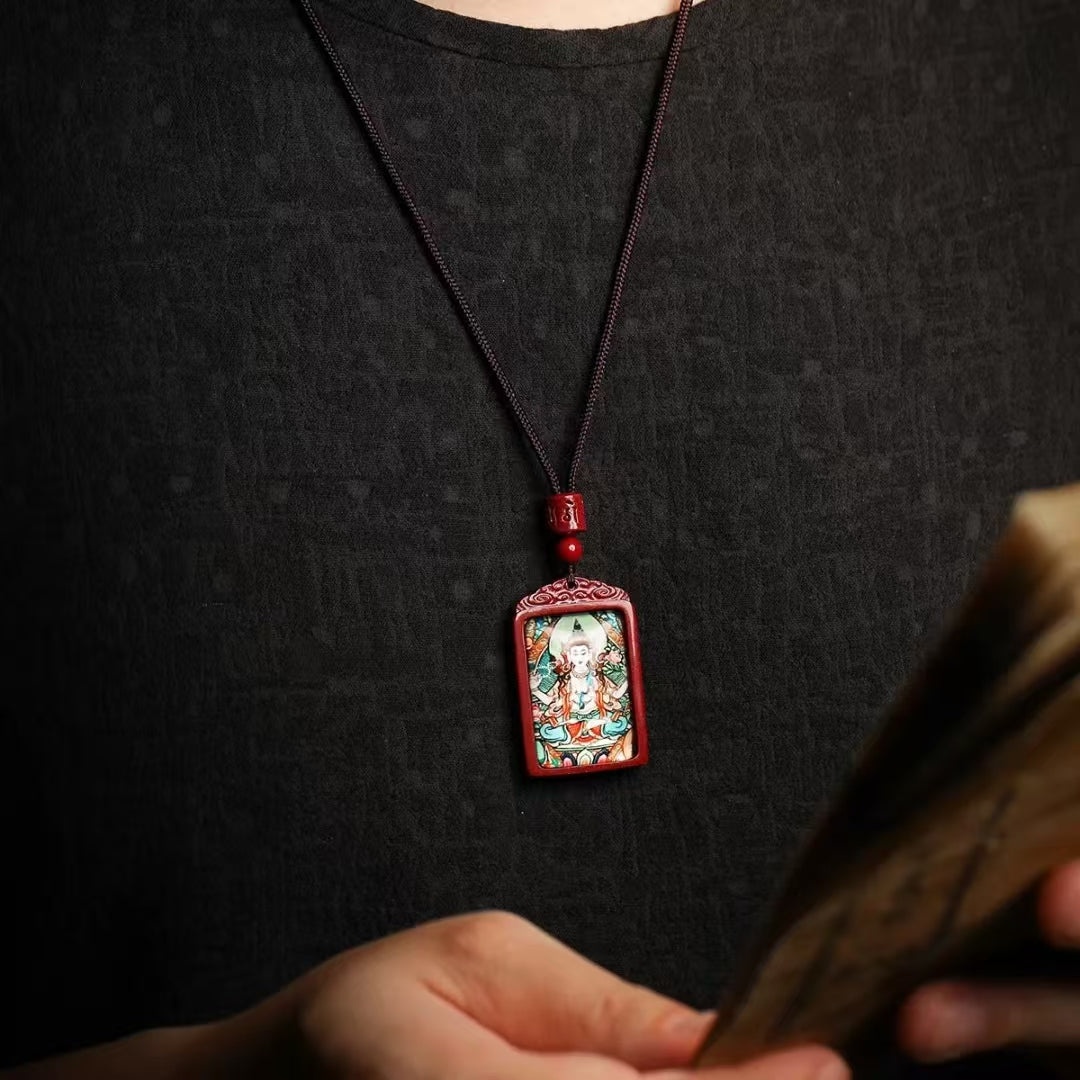A person in a black shirt showcases Joyce’s Tibetjewelry Thangka Bodhisattva Manjushri Wealth Deity Necklace—Sacred Amulet for Prosperity & Spiritual Guidance—its vivid pendant on a black cord stands out as they hold blurred papers in the foreground.